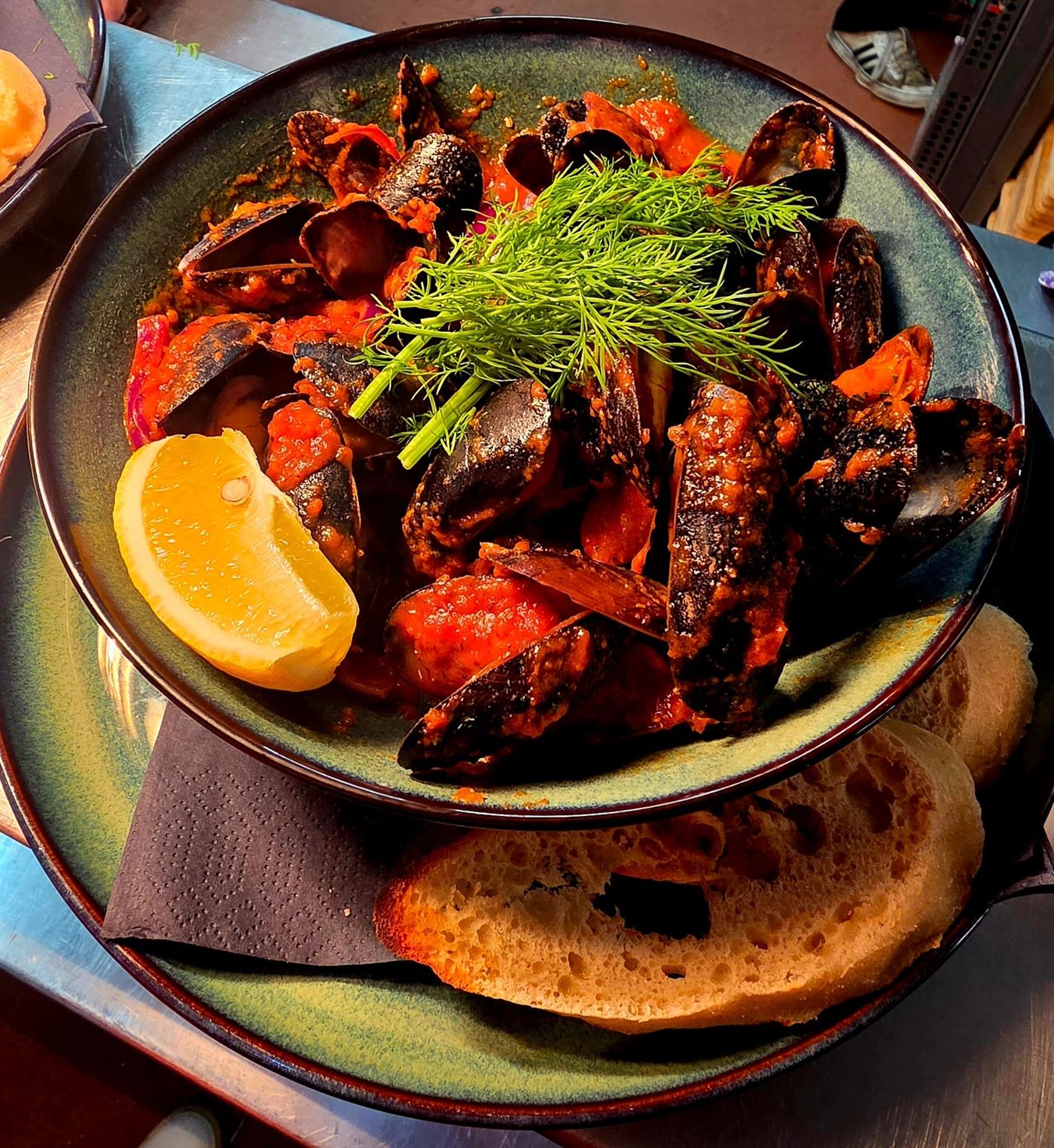 A bowl of mussels in tomato sauce with lemon and crusty bread
