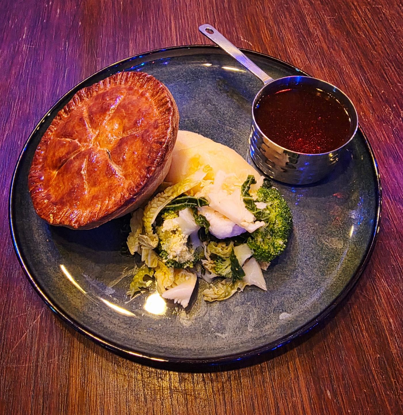 A homemade pie with mash, greens and a jug of gravy